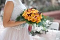 Bride in a beautiful white dress goes holding a wedding bouquet of orange roses in her hands