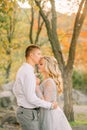 Bride with blond fair in a gentle haircut kisses her fiance at a wedding day, dressed in gray dress with transparent