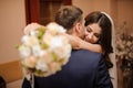 Bride with a bouquet hugs bridegroom, while he kisses her