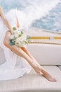 Bride with a bouquet sits on board a yacht sailing on the sea. Cropped. Faceless