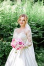Bride in classy dress with long sleeves holds pink wedding bouquet standing in the park Royalty Free Stock Photo