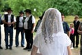 Bride with curly hair. Not face in front of camera. Brides veil. Outdoor wedding, people with hats