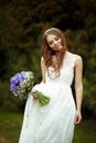 Bride daydreams standing with a violet bouquet in the park Royalty Free Stock Photo