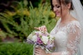 Bride in a dress standing in a green garden and holding a wedding bouquet of flowers and greenery Royalty Free Stock Photo