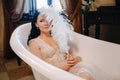 the bride, dressed in a boudoir transparent dress and underwear, lies in a vintage bathroom with a white feather in her Royalty Free Stock Photo