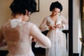 the bride, dressed in a boudoir transparent dress and underwear, stands at home in the morning by the mirror