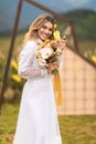 The bride, dressed in her wedding gown, stands in a lush field with a natural bouquet of flowers in her hand, beaming with joy and Royalty Free Stock Photo