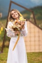 The bride, dressed in her wedding gown, stands in a lush field with a natural bouquet of flowers in her hand, beaming with joy and Royalty Free Stock Photo