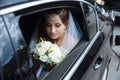 The bride is dressed in a wedding dress and veil, her head is draped with a lapel and sits in the car and admires the Royalty Free Stock Photo