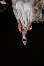 bride wears a wedding shoe on the black floor. vertical photo