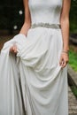 Bride in an elegant silk dress, stands and holds the dress by the edge belt decoration