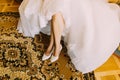 Bride in elegant white dress showing stylish shoes sitting. Oriental style carpet under her feet as background Royalty Free Stock Photo