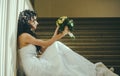 Bride in fashion white dress. Sensual woman with wedding bouquet. Woman with flowers sit on staircase. Girl with bridal