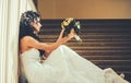 Bride in fashion white dress. Sensual woman with wedding bouquet. Woman with flowers sit on staircase. Girl with bridal Royalty Free Stock Photo