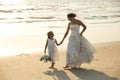 Bride and flower girl walking on beach.