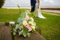 Bride flowers bouquet on wooden bench with wedding couple in blurry background Royalty Free Stock Photo