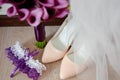 Bride garter, bridal bouquet of purple calla lilies with satin ribbon and beige women shoes on floor, copy space.