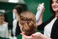 Bride getting ready for wedding. Professional hairdresser making coiffure for female client, applying hairspray in front of big