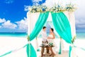 Bride giving an engagement ring to her groom under the arch decorated with flowers on the sandy beach. Wedding ceremony on