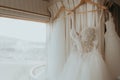 Bride gown and dresses hanging next to a window