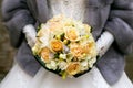 Bride in a gray fur coat holding a bridal bouquet of roses. Winter wedding