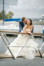 Bride and groom with a bouquet posing on a background pier with yachts