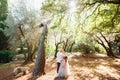 The bride and groom with a bouquet stand hugging near an unusual tree in an olive grove