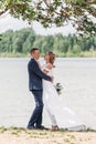 Bride and groom dance under a green tree branch by lake