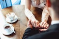 The bride and groom drinking coffee in a cafe at the round wooden table. gently holding each other`s hands Royalty Free Stock Photo