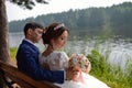 Bride and groom enjoying the beautiful landscape sitting on a bench near lake in summer Royalty Free Stock Photo