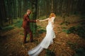 The bride and groom go through the forest hand in hand. Happy bride and groom holding hands and walking in forest on wedding day Royalty Free Stock Photo