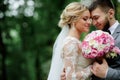 Bride and groom in grey suit look gorgeous posing in a bright summer forest