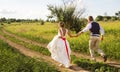 The bride and groom happily run along the path in the park. The groom holds the bride`s hand.