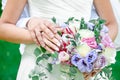 Bride and groom hold hands, sunny day, hands with wedding rings close-up on a background of a bouquet of roses and eustomas Royalty Free Stock Photo