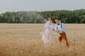 Bride and groom holding wedding champagne glasses on the background of wheat field. Happy wedding couple in wheat field Royalty Free Stock Photo