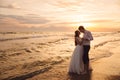 Bride and groom hugging and hold each other`s hands at beautiful sunset background. Newlyweds at wedding day on ocean Royalty Free Stock Photo