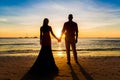 The bride and groom are kept hands on a tropical beach . Silhouette photo at sunset . Royalty Free Stock Photo