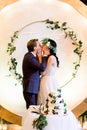 Bride and a groom kissing, standing behind their rustic wedding cake on banquet. Rustic wedding reception outdoors in Royalty Free Stock Photo