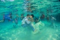 Bride and groom kissing underwater with many couples in the background