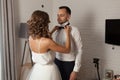 The bride and groom in the morning at the hotel on a wedding day. Dressing a newly-married couple Woman help fixing bowtie to groo