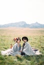 Bride and groom in plaids are sitting on a bedspread on a green lawn Royalty Free Stock Photo