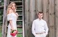 Bride and groom are posing near the old wooden house with a staircase Royalty Free Stock Photo