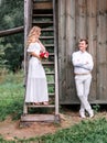 Bride and groom are posing near the old wooden house with a staircase Royalty Free Stock Photo