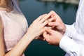 the bride and groom put on each other rings, a burgundy suit and a beige wedding dress, sunny day, a ceremony by the river Royalty Free Stock Photo