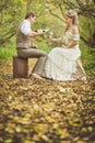 The bride and groom in a rustic style sitting at autumn forest, drink vine from glasses