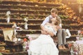 The bride and groom in a rustic style sitting on stone steps at sunny autumn forest, surrounded by wedding decor.