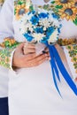 Bride and groom in shirts embroidered with sunflowers hold a bridal bouquet of blue and white chrysanthemums with blue ribbon.