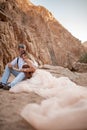 Bride and groom sit and embrace on sand in canyon against background of rocks. Royalty Free Stock Photo