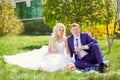 The bride and groom sit on the grass in the park, with glasses i Royalty Free Stock Photo