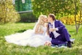 The bride and groom sit on the grass in the park, with glasses i Royalty Free Stock Photo